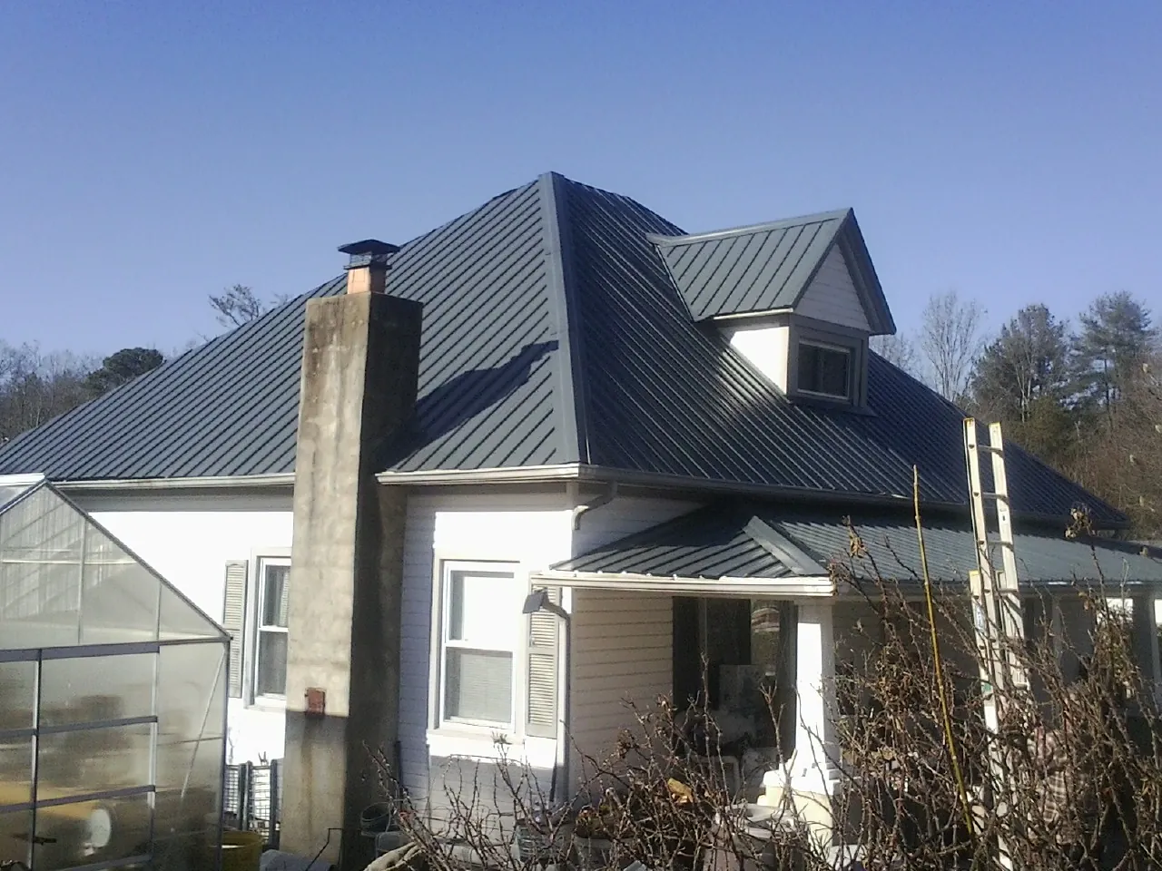Dark blue standing seam metal roof on a white farmhouse with dormer — Slate & Tile Roof Repair by Roofing Brothers in Virgin