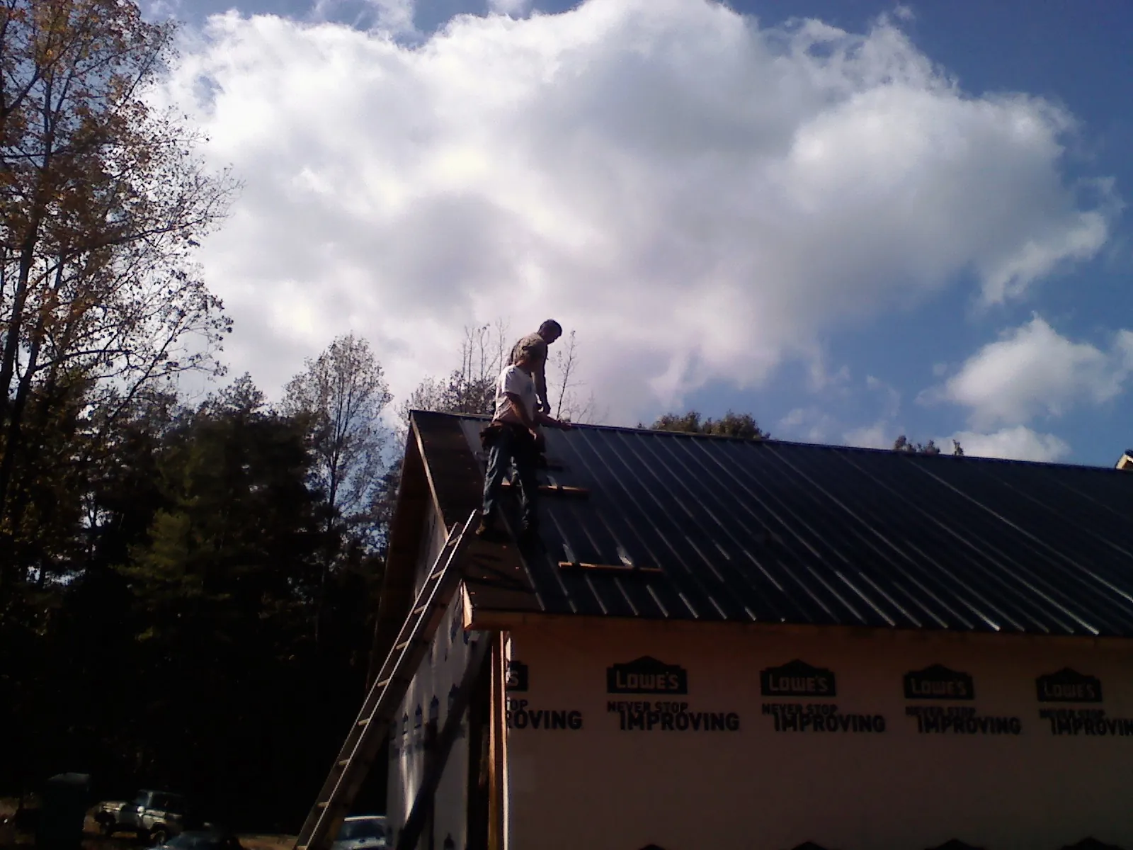 Roofer fastening dark metal panels high against a cloudy sky, from a Roof Inspection job in Virgin